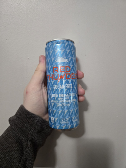 Photograph of a white person's hand holding a light blue can against a light colored wall. The can is labeled Summit Red Thunder Sugar Free. It is Aldi's version of sugar free Red Bull.