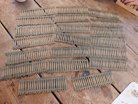 20 duck boards lying on a table, all painted in gray Brown with slightly muddy turquoise edges. They've been made of extra large stir sticks
