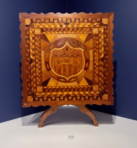 Item description:

Independent Order of Odd Fellows Marquetry Table, 1933
Probably Islip, New York / Wood
Collection American Folk Art Museum, New York, Gift of Kendra and Allan Daniel, 2015.1.160 (ames J. Crozier, a carpenter from Islip, New York, made this intricately decorated marquetry table Is surface features a number of fraternal symbols, but it is the prominent letters "FLT" and "iOOF and the three-link chain that mark this as an Odd Fellows object. The initials for "Friendship," "Love," and "Truth" served to remind lodge members of the ritual teachings from the Initiatory Degree: like the chain, they were bound together in those virtues. The all-seeing eye symbolizes the omniscience of God, and the heart in hand signifies candor and sincerity.
