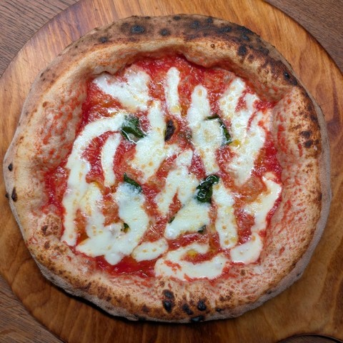 A Pizza Napoletana with an big and airy crust on a wooden plate. It's the queen of Pizza, a Margherita.
