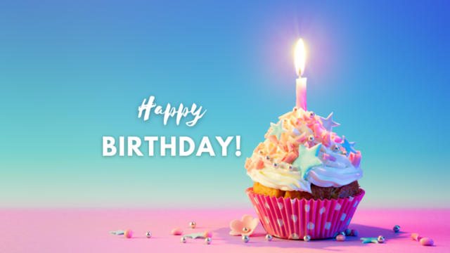 The image features a vibrant birthday cupcake with a single lit candle on top. The cupcake is adorned with white frosting, colorful sprinkles, and star-shaped decorations. It is placed in a pink polka-dotted cupcake liner. The background is a gradient of blue and pink, creating a cheerful atmosphere. Scattered around the cupcake are small, colorful sprinkles and a few flower-shaped decorations. The text "Happy BIRTHDAY!" is prominently displayed in white, with "Happy" in a cursive font and "BIRTHDAY!" in a bold, uppercase font. The overall composition is festive and celebratory, with a focus on the cupcake as the central element.