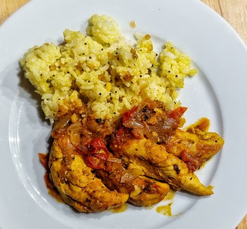 a white plate with yellow rice on the top, and orange xhicken renders with a reddish sauce below. The rice shows mustard seeds, curry leaves and bits of peanuts and lentils
