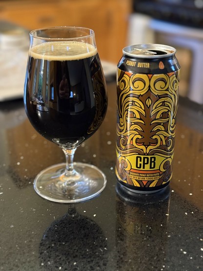 A snifter glass of dark beer. The pint can shows stacked peanut butter cups in brown yellow and orange with vine-like swirls tying them together