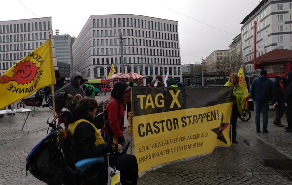 Kundgebung vor dem Bremer Hbf. Transparent Tag X Castor stoppen, Personen die es halten und Anti-Atom Fahnen.
