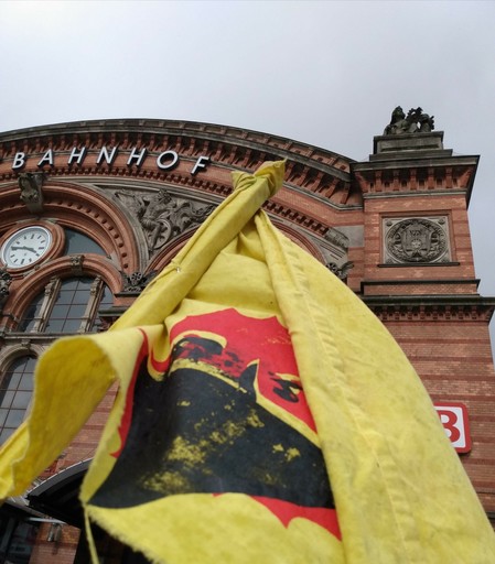 Fahne mit vermumter Sonne vor dem Gebäude des Bremer Hbf.
