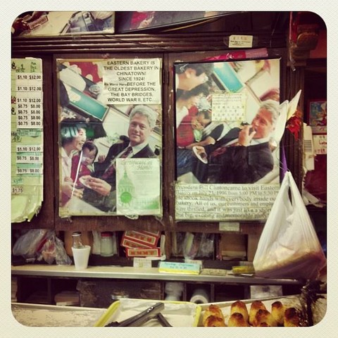 Large photos of President Bill Clinton sampling the food at Eastern Bakery, among chaotic and cluttered back counter.