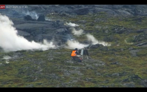 Mehrere Menschen in Schutzwesten hantieren an Meßgeräten während im Hintergrund die Lava näher kommt.