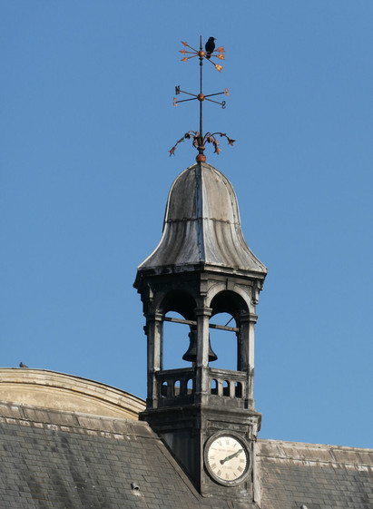 A crow sits atop a weather-vane on a clock tower at Place Des Vosges, Paris, France. March 2025.