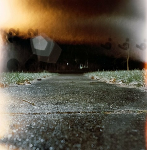 A wet sidewalk shot at night with light leaks and the film backing present due to a film defect.