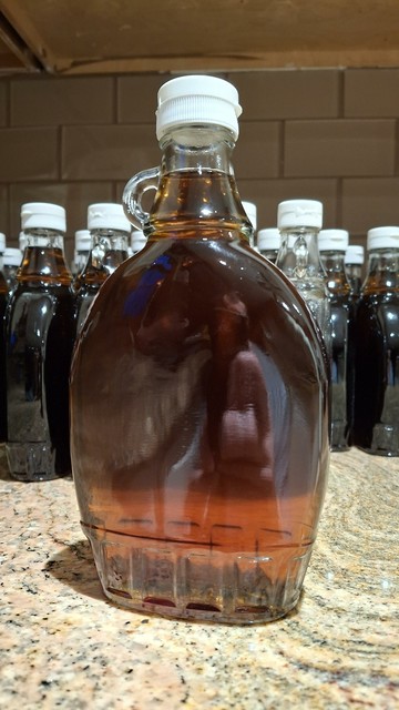 A single bottle, with others in the background. Syrup is dark and clear.