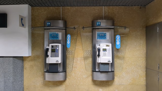 Dois telefones públicos numa parede, bem perto um do outro.