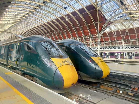 Two green (with yellow nose) trains sat side-by-side at station.