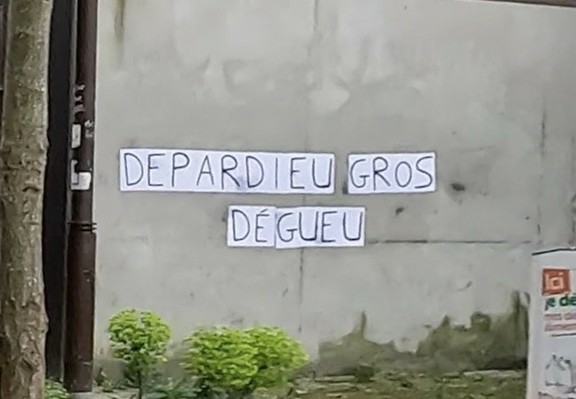 Feuilles blanches collées sur un mur gris pour former le message en lettres capitales « DEPARDIEU GROS DEGUEU »