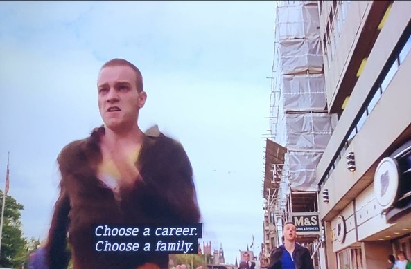 A young Ewan McGregor (in his early 20s) running brown shirt open down a store lined street. Head shaved, deep-set dark circles around his eyes. He does not look well. 
Subtitles read: Choose a career.
Choose a family.