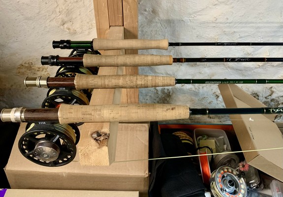 Several fly rods with reels hang on a wooden rack.