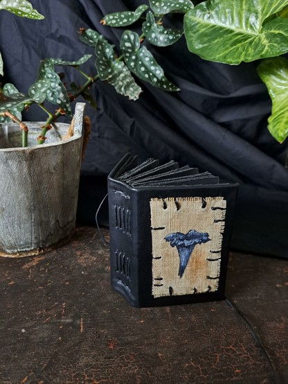 A small black leather sketchbook with an original horn of plenty mushroom painting sewn on the cover.