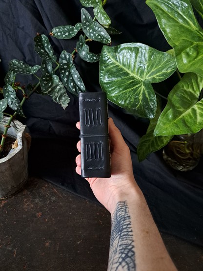 A hand holding the black pocket size journal showing only the spine and the stitching made by hand.