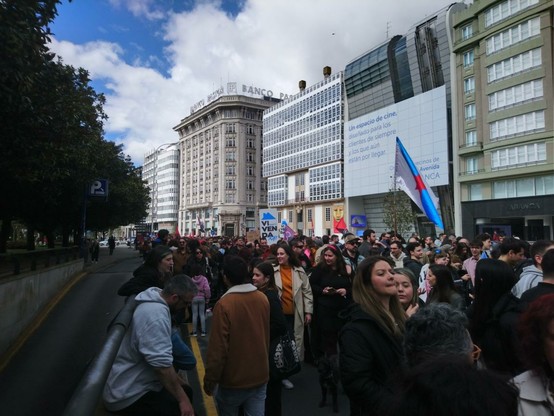 Manifestación por la vivienda, ocupando la calle completa. En primer plano los manifestantes con pancartas y banderas, al fondo el antiguo banco Pastor (ahora Santander) y el resto de edificios del centro.