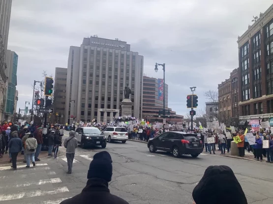 A city square with lots of people filling the square and sidewalks. There are police cars there as well.