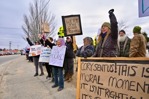 People standing on a sidewalk holding signs which include, "We're the good trouble".