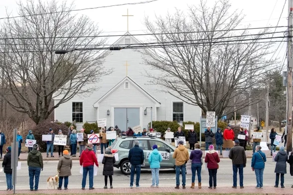 People gathered on both sides of a street in front of a church.