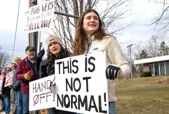 People holding up signs. Some of the signs read: "Rob vets today Elon? Hell No!", "Hands Off" and "This is not normal."