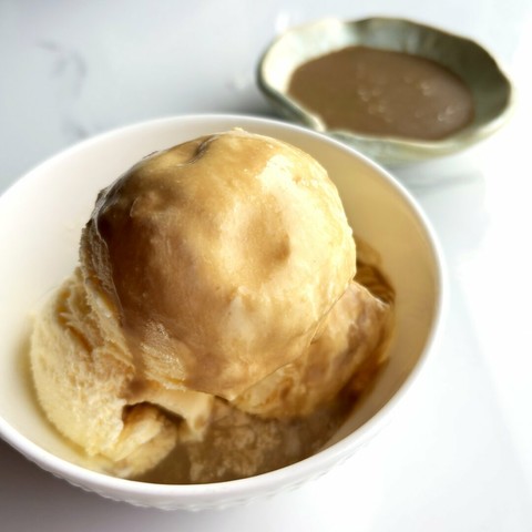 A bowl of vanilla ice cream with spoonfuls of Salty Guinness Maple Caramel over it.
