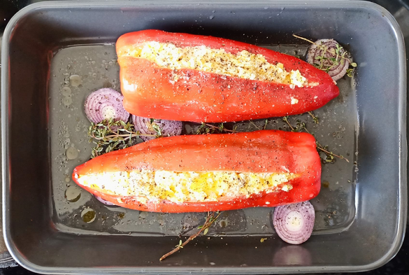 In einer Auflaufform 2 große gefüllte rote Spitzpaprika auf Zwiebelscheiben.