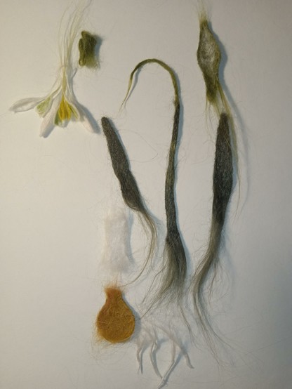 On a white background lie parts of the craft, made from nettles using needle felting. This will be a bookmark in the form of a snowdrop. Thank you for your attention!