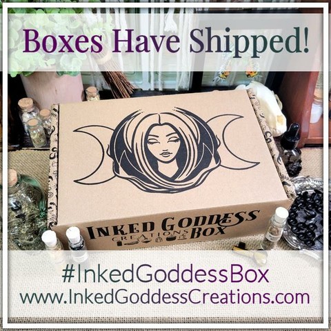 A rectangular brown cardboard box is set diagonally on a burlap-covered table, surrounded by witchy items like gemstones, candles, and vials of herbs. The box features our exclusive brand packaging. The text across the top reads, "Boxes Have Shipped!" The Inked Goddess Creations Box is an exclusive product from Inked Goddess Creations.