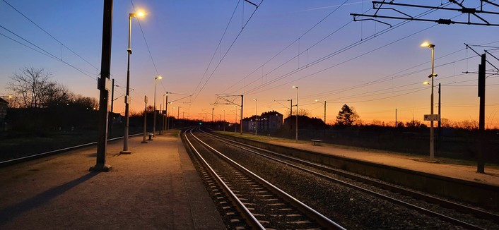 Quai de gare au lever de soleil. Les rails, parallèles, se croisent à l'infini, au loin.