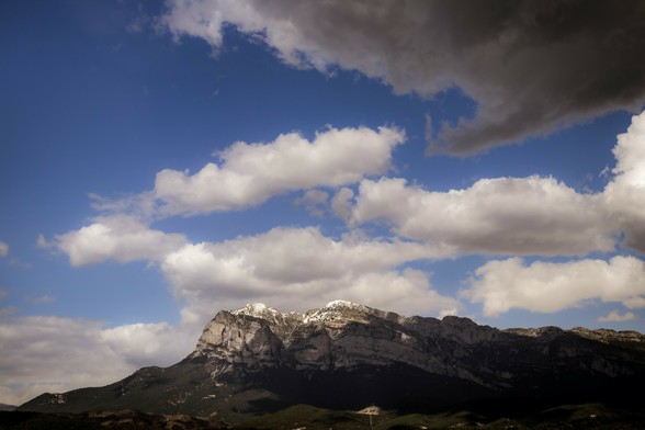 Horizontal photograph where you can see a mountain (Peña Montañesa, located in Aínsa, Spanish Pyrenees) at the bottom covered by some shadows coming from the clouds at the top.