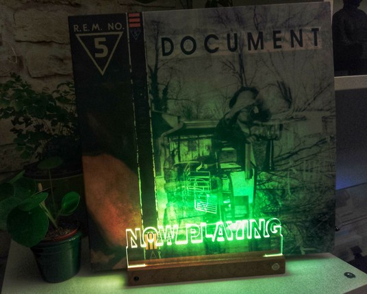 In einem kleinen Ständer steht das Albumcover von Document von R.E.M. Das Album wird von einem grünen Schriftzug "Now playing" beleuchtet.