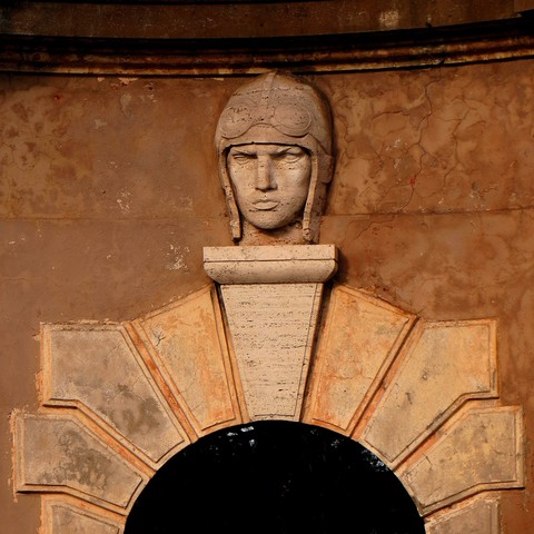 Picture of an arched entry, framed with large stucco stones. Above the keystone, a travertine sculpture of an aviator.