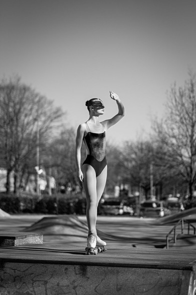 Portrait einer Rollkunstläuferin, die im Skaterpark auf einer Halfpipe steht, in Richtung Sonne schaut und sich mit einer Hand die Sonne von den Augen abhält.