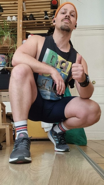 A man in shorts and athletic wear, crouching down, giving a thumbs up to the camera
