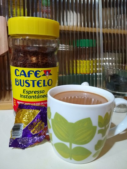 This morning's coffee mug sitting on my countertop next to an empty Cadbury's Caramel Egg foil wrapper and a jar of Café Bustelo instant espresso. The mug is white with green Scandinavian folk art style flowers on it, appropriate for Spring.