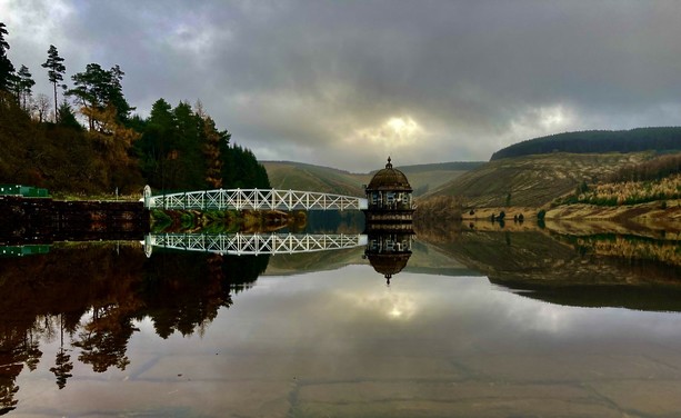 The pumping station at Tala reservoir reflected in an almost still water against a moody sky - just before a swim.