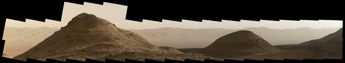 An ochre toned mosaic capturing a Martian landscape. This panoramic view features two landmark geological formations: the Gould Mesa is the highest standing butte on the left and the Wilkerson Butte is on the right. The wall of the rim of Gale Crater is seen in the background at a distance of 10 kilometers.