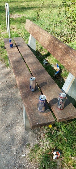 Met de lente komen ook de mensen weer. 

Houten bankje in "mijn" parkje. 
Op het bankje vier achtergelaten lege blikjes her en der. Op de grond papieren verpakking.