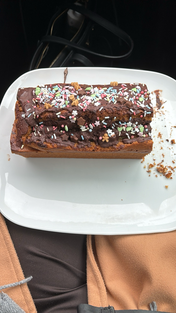 Auf dem Bild ist ein veganer Marmorkuchen auf einem weißen Teller. Auf dem Kuchen ist eine vegane Schokoglasur mit vielen bunten Streuseln.