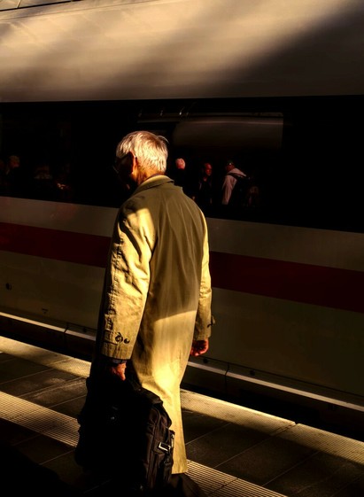 Photo of an elder passenger in the sunlight; a train behind him is in the shadow.