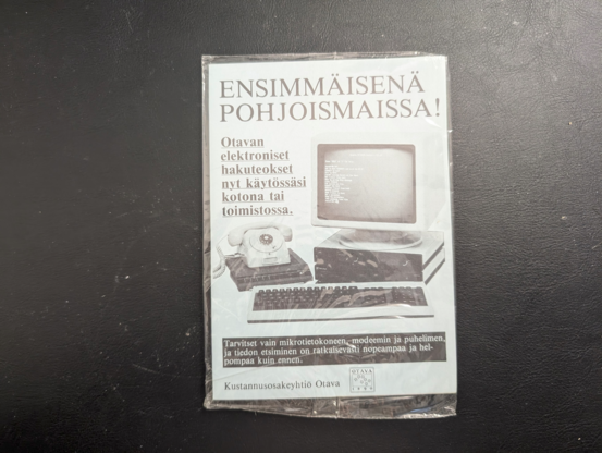 Muoviin kääritty mainos: sinisellä paperilla taiteltu A6:ksi: Ensimmäisenä pohjoismaissa! Otavan elektroniset hakuteokset nyt käytössäsi kotona tai toimistossa. Tarvitset vain mikrotietokoneen, modeemin ja puhelimen, ja tiedon etsiminen on ratkaisevasti nopeampaa ja helpompaa kuin ennen.