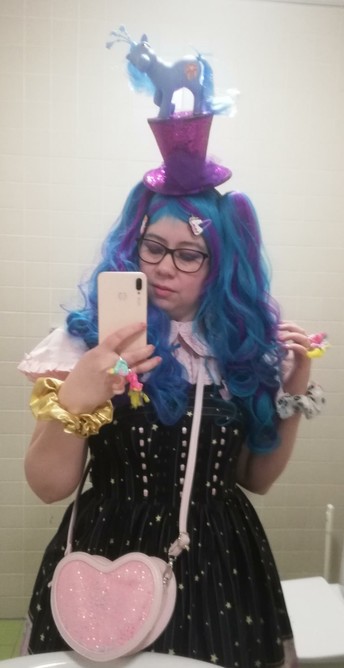 Vessaselfie poniteemaisessa lolitatyylisessä asussa. Minisilinterin päällä pikkuponilelu, sormuksissa pieniä ponileluja, päässä turkoosivioletti pitkä peruukki jossa sivuilla kiinnitettävät saparot.