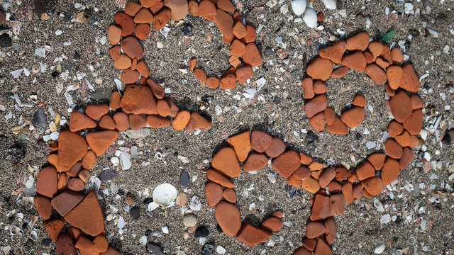 A close up detail view of an ampersand made by arranging worn terracotta tile fragments on the beach.