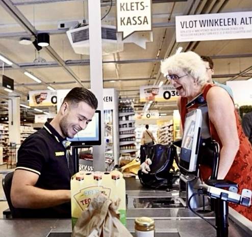 An elderly enjoying a chat with the cashier at a supermarket-both laughing & smiling.