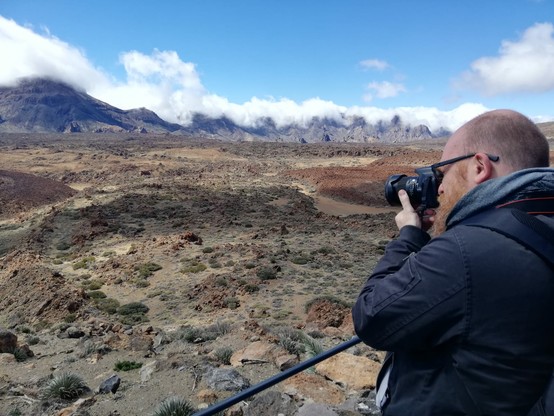 Un uomo che fotografa un paesaggio vulcanico ampio e spoglio.
