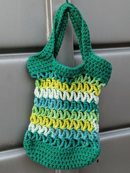 A mini crochet market bag that is green, turquoise, yellow, and white.