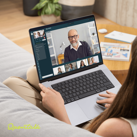 Eine Person sitzt auf einem Sofa und hat eine Laptop auf dem Schoß. Im Zentrum des Bildes sieht man den Bildschirm, der eine laufende OpenTalk-Konferenz mit mehreren Teilnehmenden zeigt.