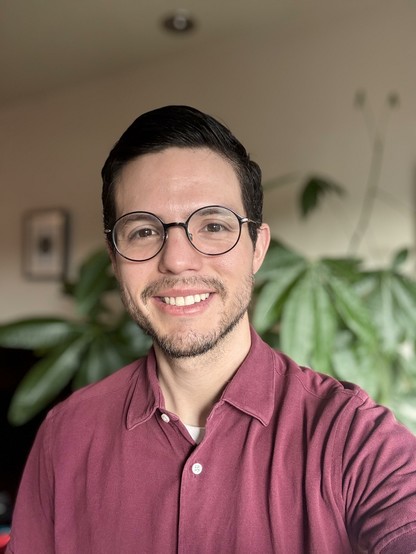 Selfie wearing a burgundy shirt, some of my house plants are visible in the background.